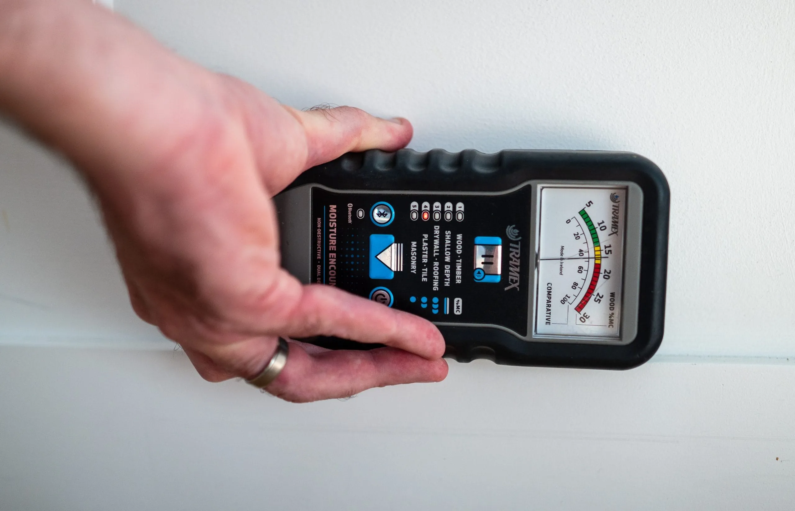 Close-up of a Top Tier building inspector using a Tramex moisture meter on a wall to detect concealed water damage and mold risks